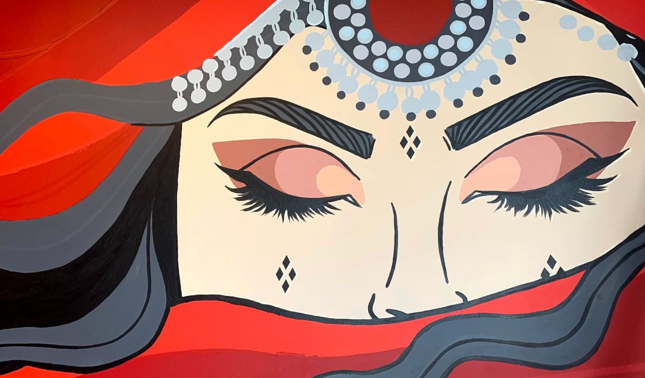 Close-up of Across the Veil: the woman's closed eyes under a beaded headpiece, her face wrapped in the red veil