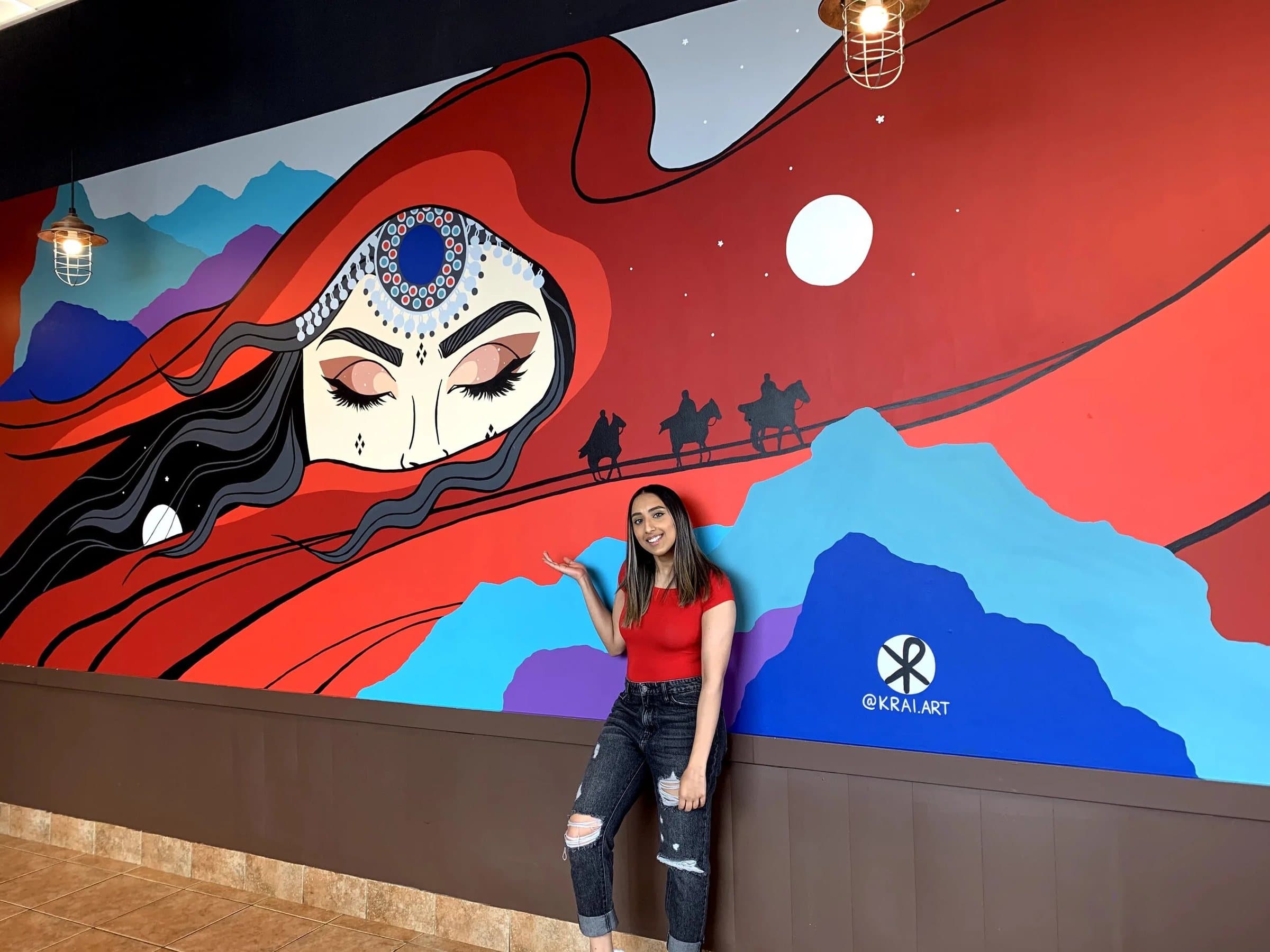 Kiran Rai with the finished Across the Veil mural, camel rider silhouettes within the red veil