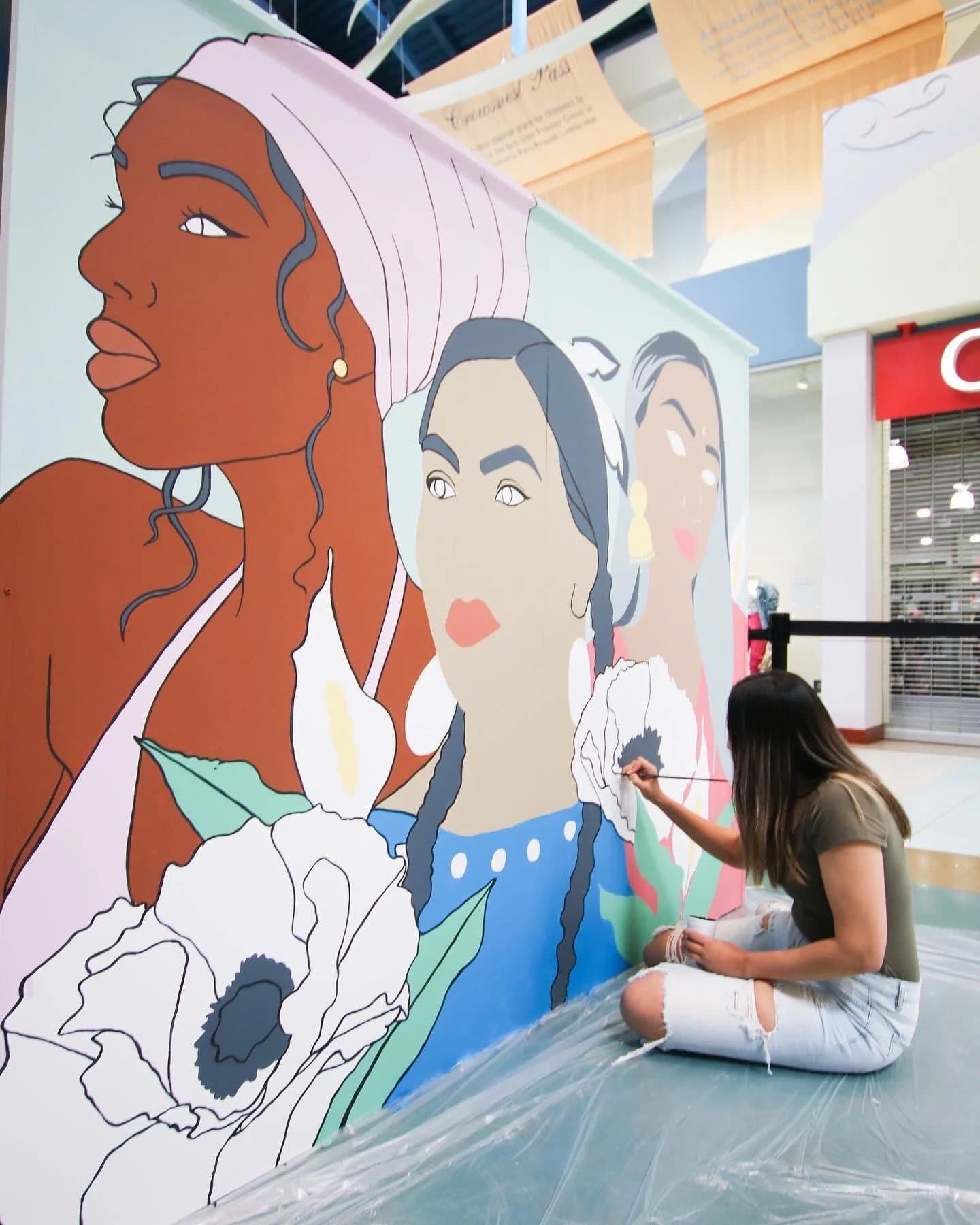 Kiran Rai painting the Co-Existence mural at CrossIron Mills, warm earth tones with cobalt blue accents