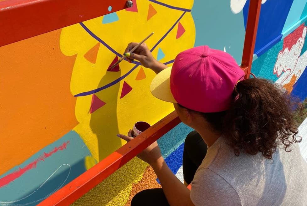 SAWA in progress: a painter in a pink cap adding the bunting to the yellow llama