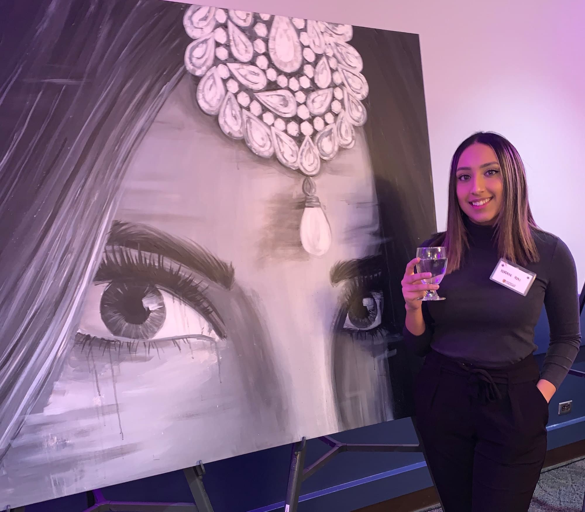 Kiran Rai-Bhullar beside the 2017 Blood Diamonds painting at the Am I Racist? event, University of Calgary