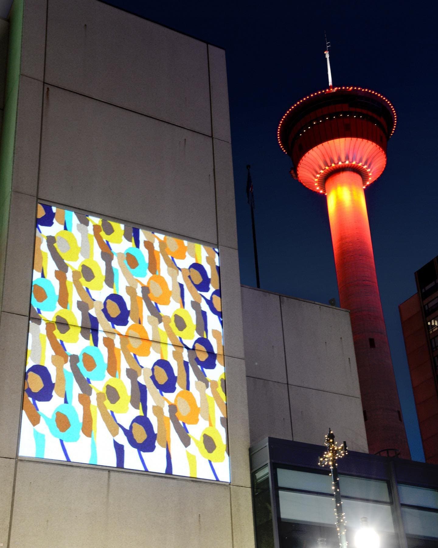Long Live Women Farmers projected onto the Glenbow Museum at night, the Calgary Tower lit red behind it