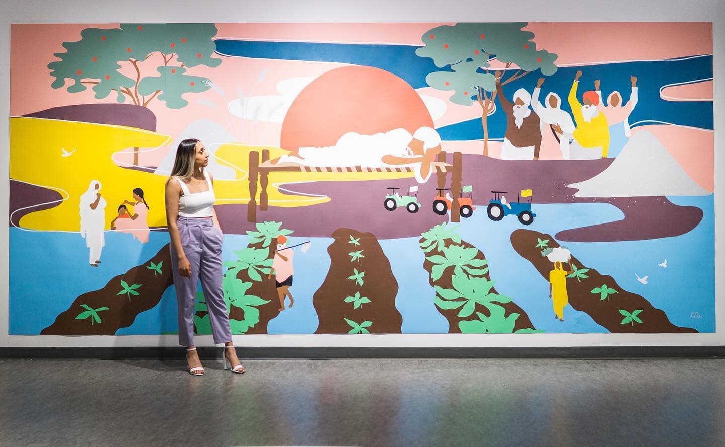 Kiran Rai-Bhullar beside Love for Humanity, a mural of farmers working the land under a rising sun