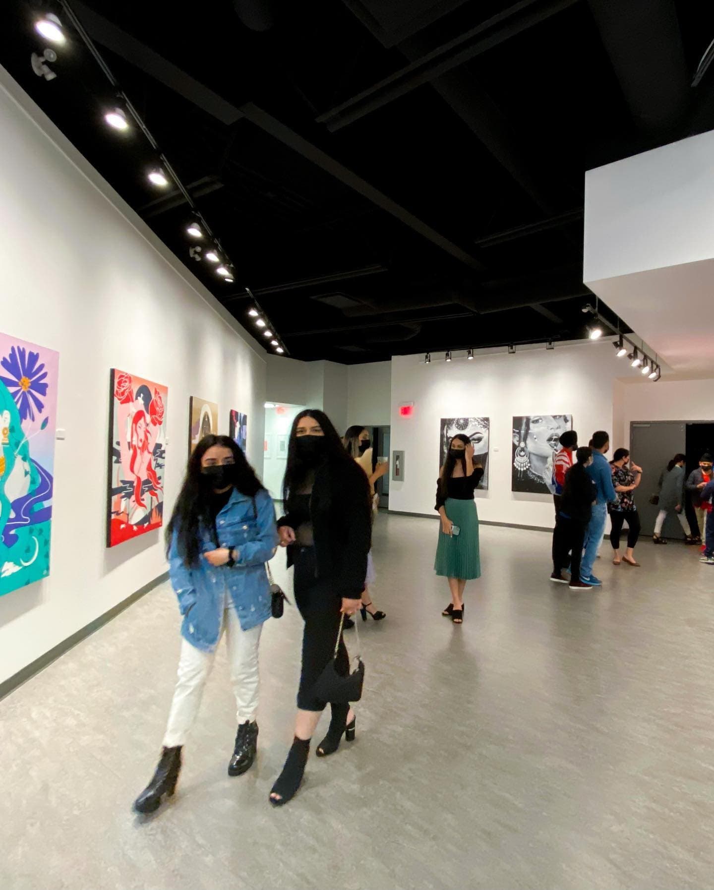 Visitors walking through the exhibition, the four paintings on the wall to the left