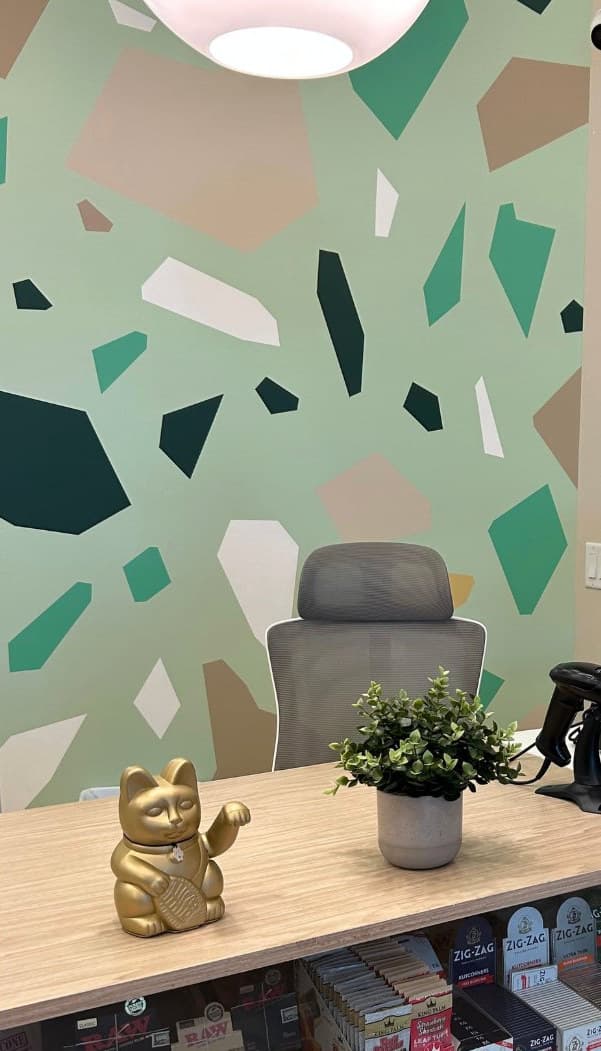 Mosaic Earth up close: terrazzo shapes on the mint wall, with a gold lucky cat and a plant on the counter