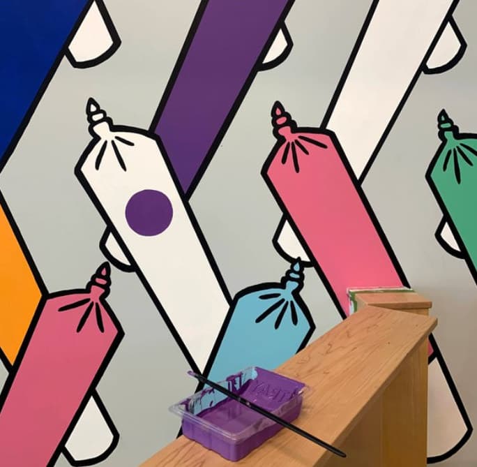 Close-up of Rainbow Doobies: outlined joints in pink, blue and white, a paint tray on the ledge below