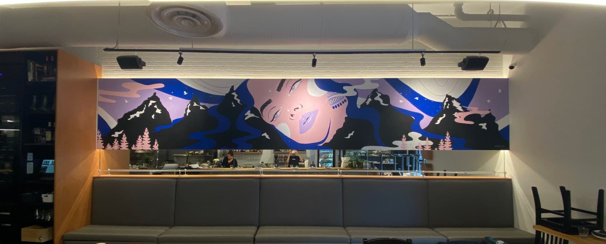 Uprooted above the banquette at UNA Pizza + Wine in Bridgeland, Calgary: a woman's face among dark peaks and blue rivers