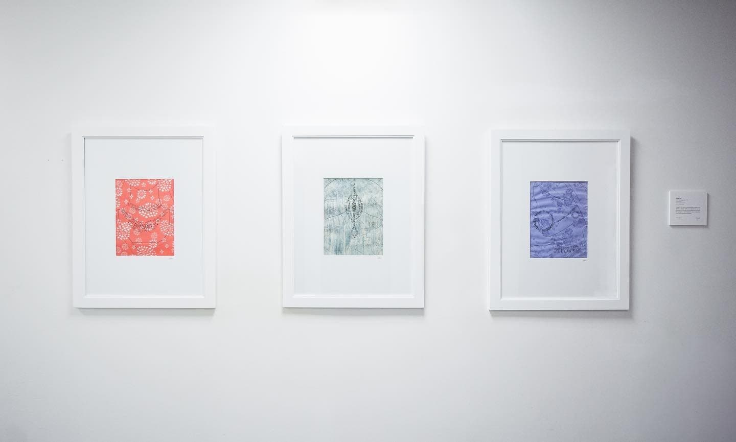 The three I Am the Diaspora prints in white frames on a gallery wall, in coral, sage and violet