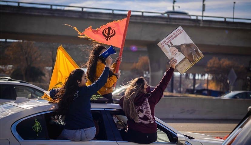 Protesters riding on a car at a farmers’ rally with flags and a megaphone, one wearing the No Farmers No Food hoodie