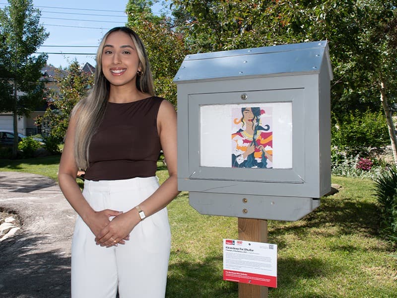 Kiran Rai-Bhullar standing beside the Northeast Mini Galleries box that held Threads of Resilience, with the exhibition label below